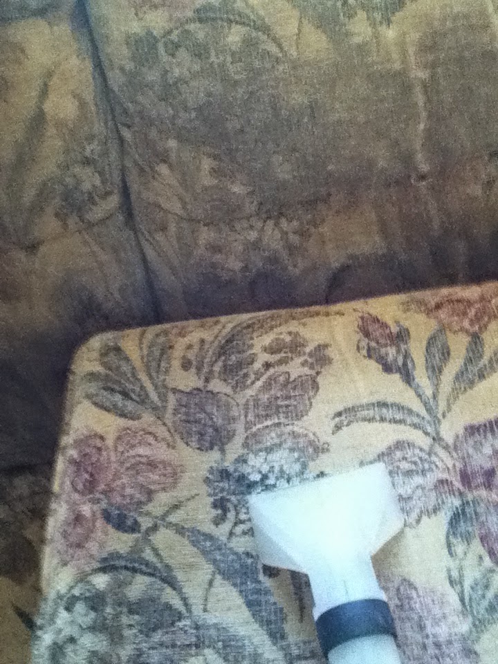 The upholstery tool cleaning the arm of a floral fabric sofa